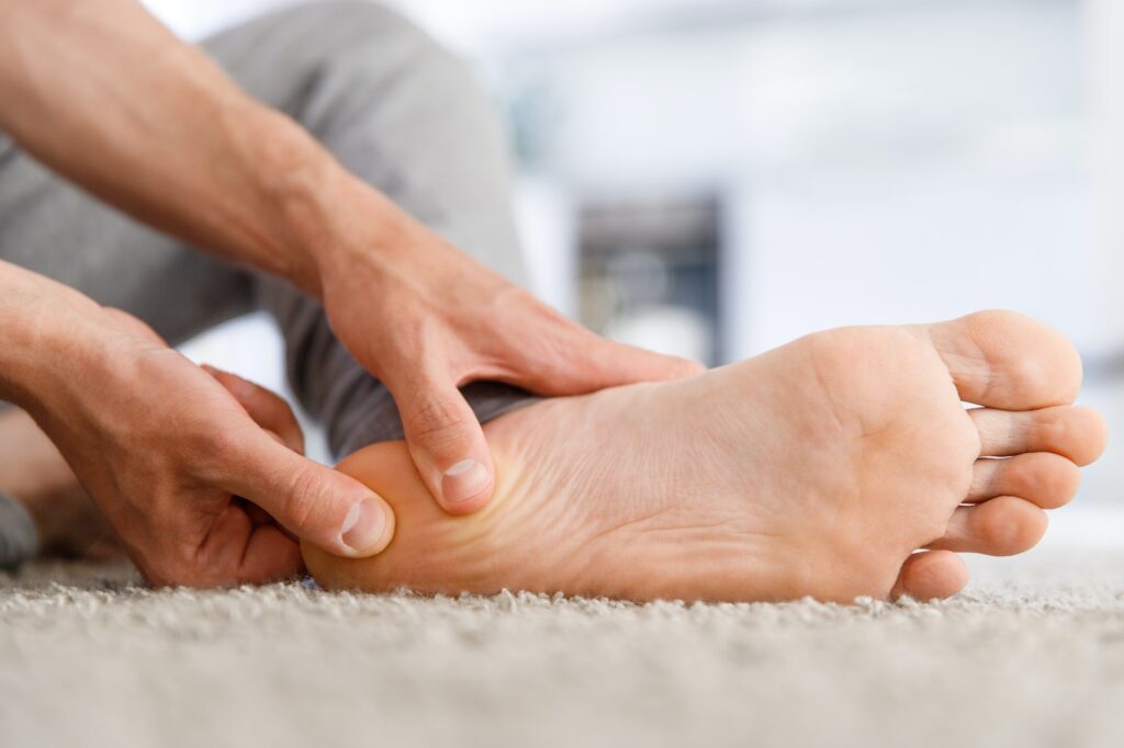 A man sits on the floor, feeling pain in his foot and massaging it.