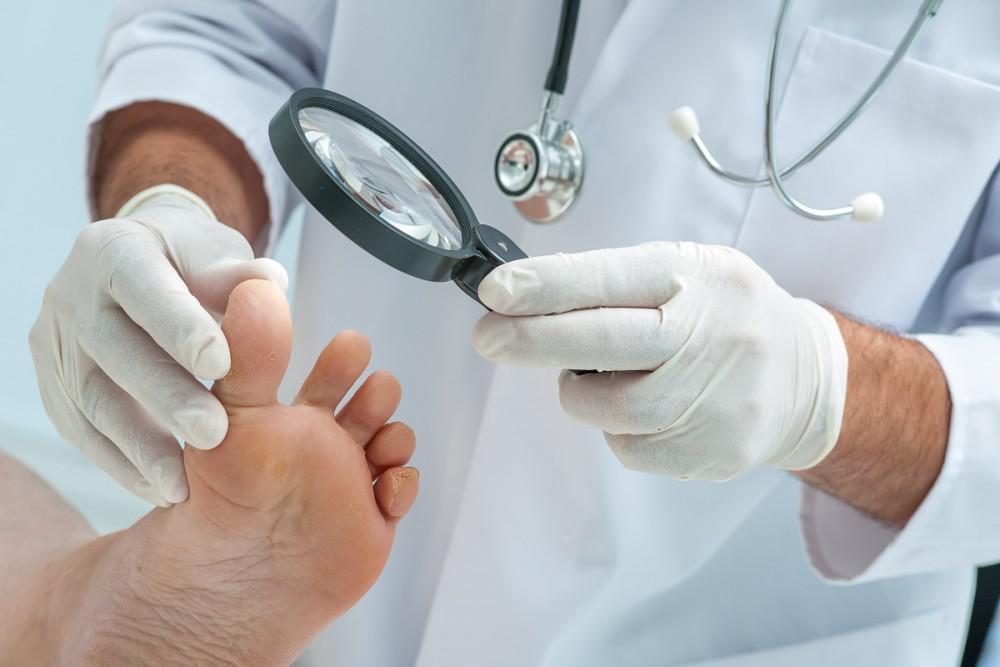 A doctor uses a magnifying glass to examine his patients' feet.