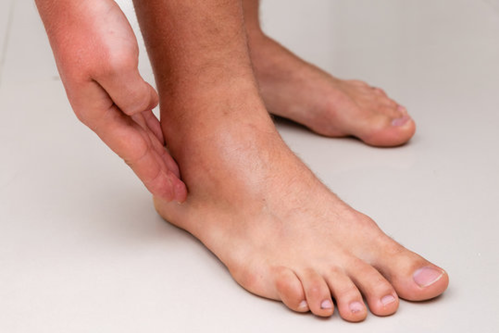 A person with tendon problems touching his ankle with a white background.