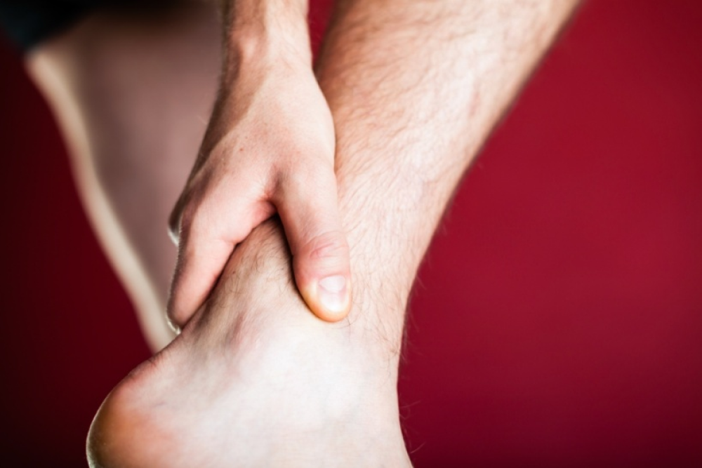 A man touched his foot's tendon area, causing pain.