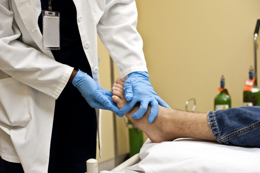 A doctor examines a patient's foot with a glove hand.