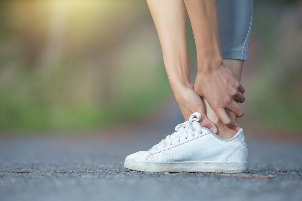 A woman feels discomfort in her ankle caused by a tendon problem when she touches it with a white shoe.